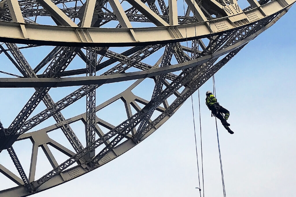 Rope access operative suspended beneath large steel truss structure