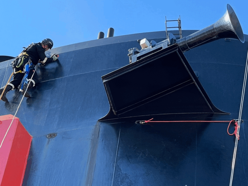 Rope access technician inspecting and maintaining ship funnel and superstructure