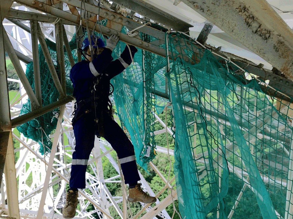 Rope access operative installing debris netting and edge protection beneath a structure